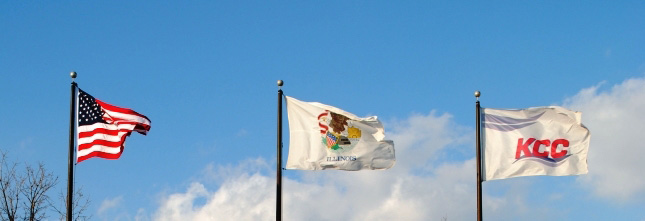 United States, Illinois, and KCC flags at full-staff against a blue slightly cloudy sky
