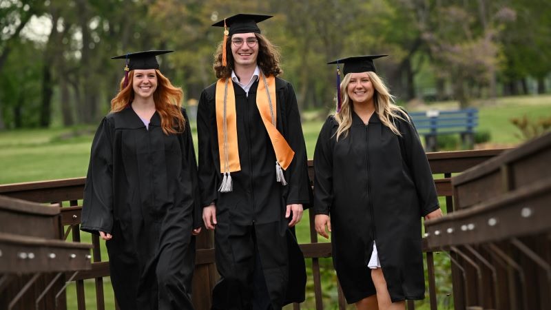 Three graduates of 2022 walking up a platform outside